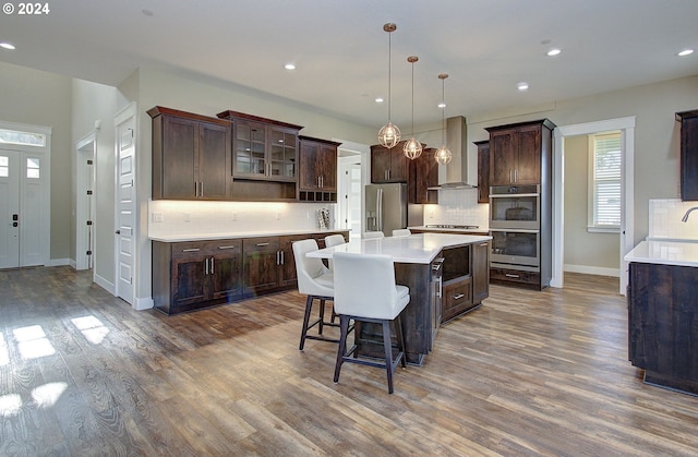 kitchen with pendant lighting, a center island, dark wood-type flooring, wall chimney exhaust hood, and stainless steel appliances