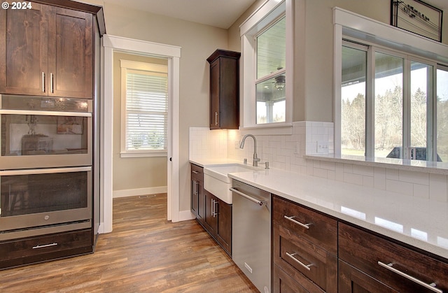 kitchen with sink, decorative backsplash, light wood-type flooring, dark brown cabinetry, and stainless steel appliances