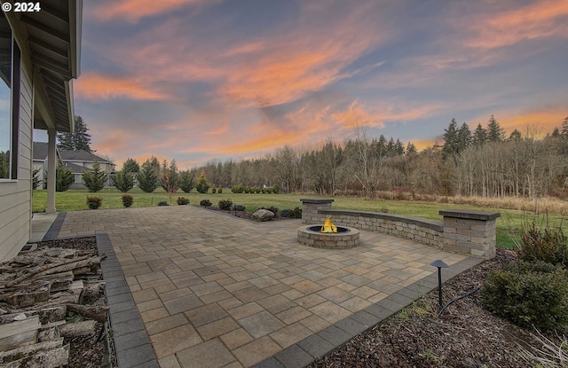 patio terrace at dusk featuring an outdoor fire pit and a lawn