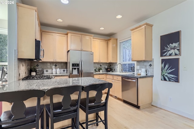 kitchen featuring light stone countertops, sink, stainless steel appliances, light hardwood / wood-style floors, and decorative backsplash