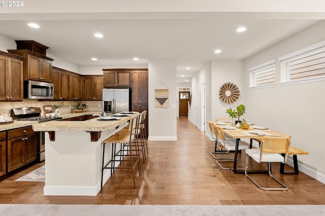 kitchen featuring decorative backsplash, a breakfast bar area, appliances with stainless steel finishes, a kitchen island with sink, and light hardwood / wood-style floors