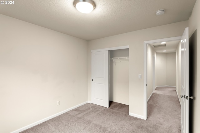 unfurnished bedroom featuring a textured ceiling, light colored carpet, and a closet