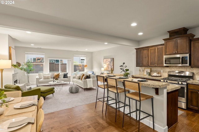 kitchen with backsplash, dark hardwood / wood-style flooring, stainless steel appliances, dark brown cabinetry, and a breakfast bar