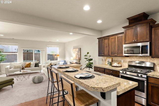 kitchen with hardwood / wood-style flooring, stainless steel appliances, a breakfast bar area, and backsplash