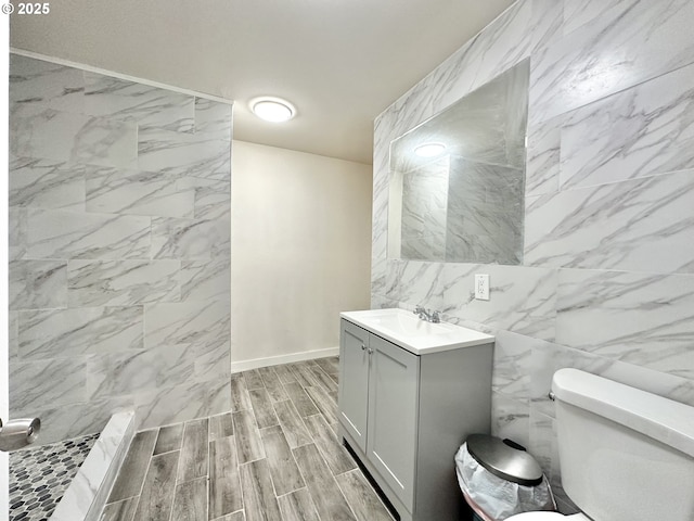 bathroom with walk in shower, vanity, tile walls, and toilet