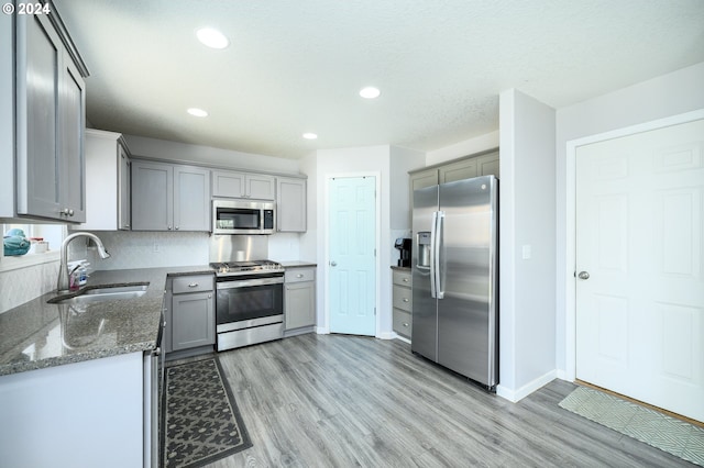 kitchen with gray cabinetry, a sink, appliances with stainless steel finishes, light wood-type flooring, and dark stone countertops