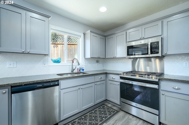 kitchen with dark stone counters, appliances with stainless steel finishes, a sink, and gray cabinetry