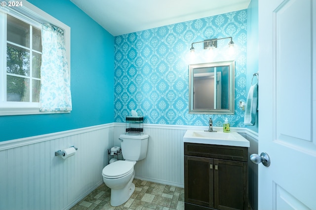 half bathroom with toilet, a wainscoted wall, wallpapered walls, and vanity