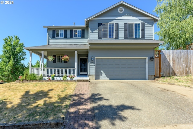 traditional home with covered porch, a garage, fence, driveway, and a front yard