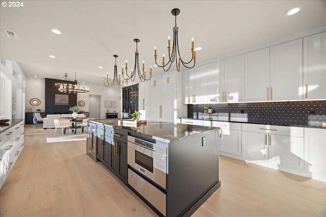 kitchen featuring white cabinetry, tasteful backsplash, decorative light fixtures, a center island, and dark stone countertops