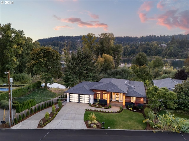 view of front of home featuring fence, a wooded view, driveway, a front lawn, and a garage