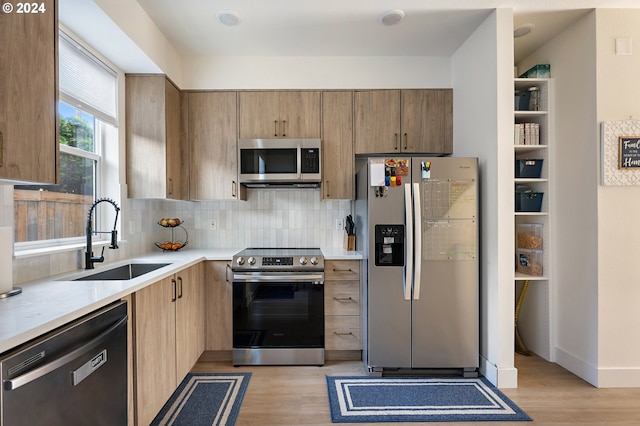 kitchen with stainless steel appliances, sink, light wood-type flooring, and decorative backsplash