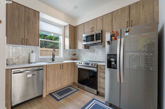 kitchen with tasteful backsplash, stainless steel appliances, sink, and light wood-type flooring