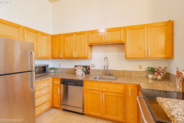 kitchen with stainless steel appliances, sink, light stone countertops, light tile patterned floors, and a towering ceiling