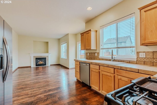 kitchen featuring appliances with stainless steel finishes, dark hardwood / wood-style floors, a tiled fireplace, sink, and tile countertops