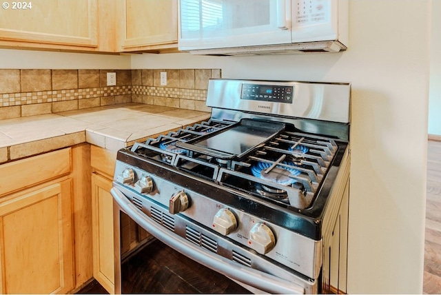 kitchen with tile counters, hardwood / wood-style flooring, stainless steel gas stove, backsplash, and light brown cabinetry