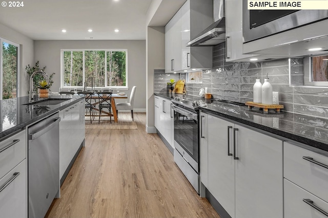 kitchen with light hardwood / wood-style floors, wall chimney exhaust hood, white cabinets, sink, and appliances with stainless steel finishes