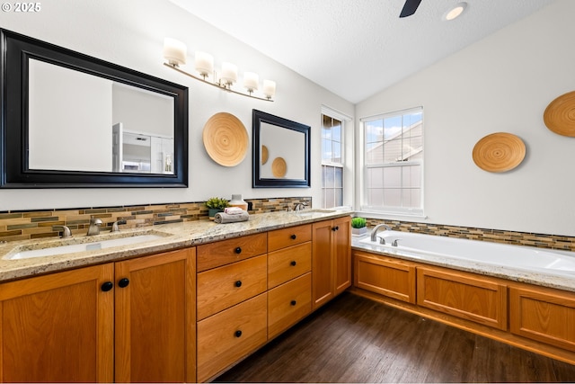 bathroom featuring vaulted ceiling, a textured ceiling, vanity, a tub, and hardwood / wood-style floors