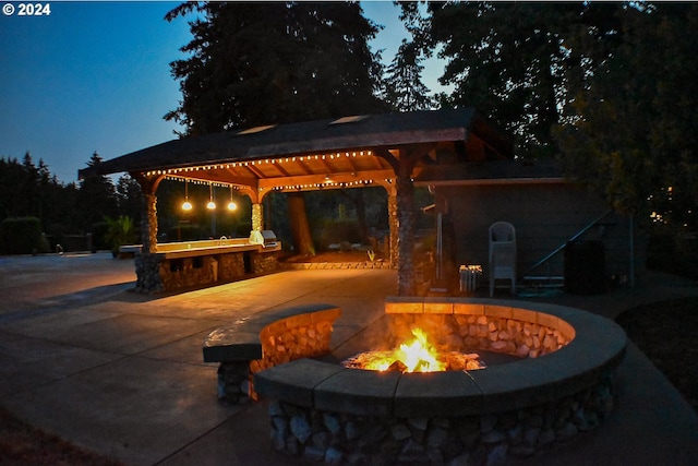 patio terrace at dusk with an outdoor bar, a gazebo, an outdoor fire pit, and area for grilling