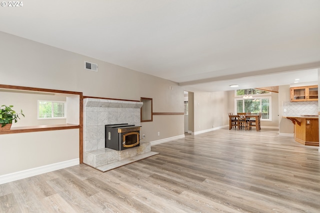 unfurnished living room featuring light wood-style floors, a wood stove, visible vents, and baseboards