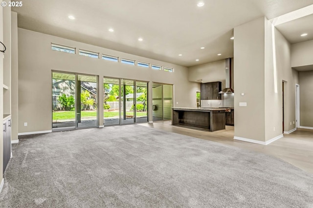 unfurnished living room featuring a towering ceiling, recessed lighting, baseboards, and light carpet