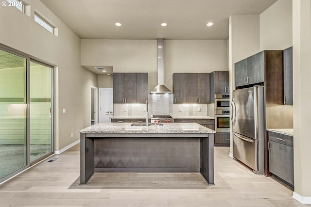 kitchen featuring appliances with stainless steel finishes, decorative backsplash, a sink, a kitchen island with sink, and dark brown cabinetry