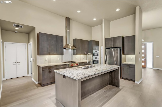 kitchen with a sink, wall chimney range hood, light wood-style floors, tasteful backsplash, and dark brown cabinets