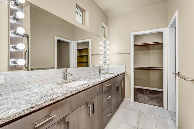 full bath featuring double vanity, a spacious closet, baseboards, and tasteful backsplash