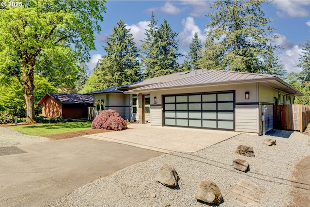 view of front of home with an attached garage, concrete driveway, a standing seam roof, fence, and metal roof