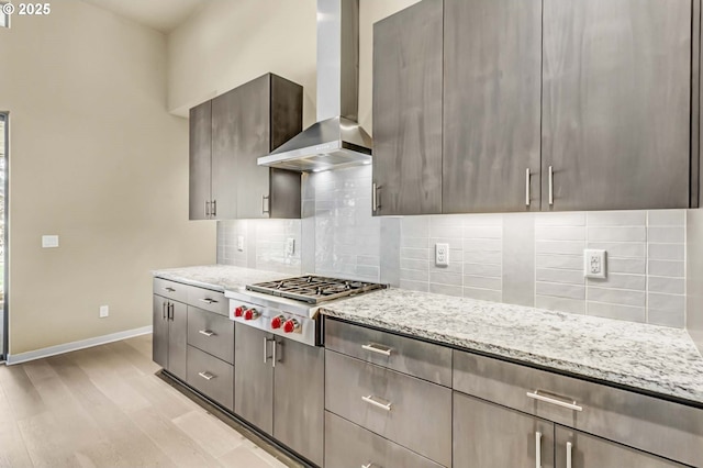 kitchen featuring wall chimney range hood, stainless steel gas cooktop, baseboards, and light stone counters