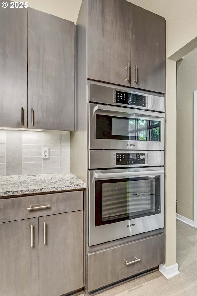 kitchen featuring double oven, light stone counters, decorative backsplash, and baseboards