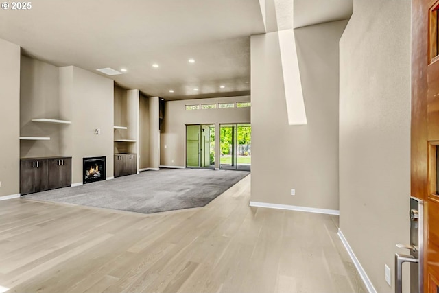 unfurnished living room with wood finished floors, baseboards, recessed lighting, a warm lit fireplace, and built in features