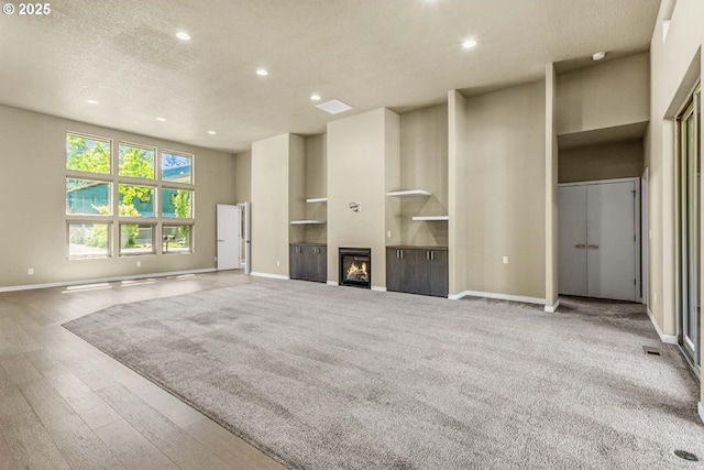 unfurnished living room with recessed lighting, baseboards, a textured ceiling, wood finished floors, and a glass covered fireplace