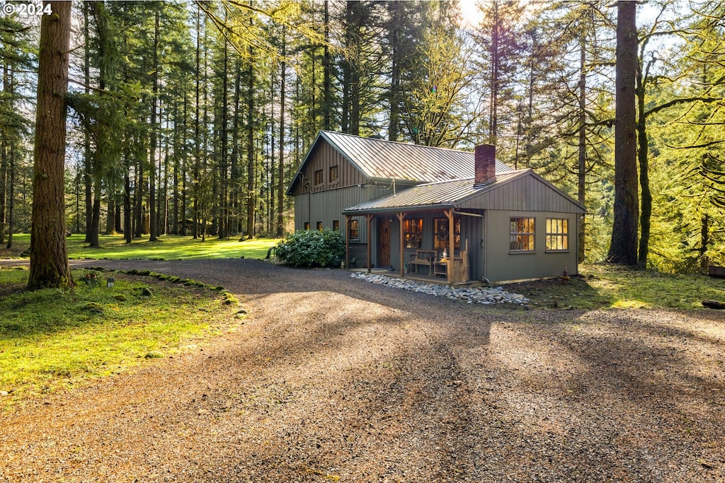 view of front of house featuring metal roof, driveway, a standing seam roof, and a chimney