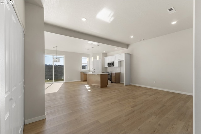 unfurnished living room featuring light wood-style flooring, recessed lighting, a sink, visible vents, and baseboards