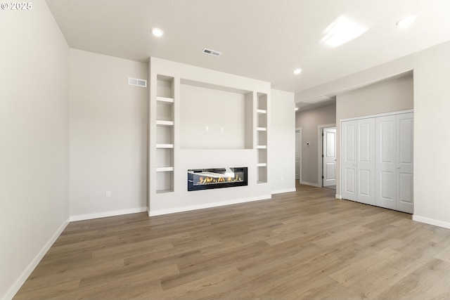 unfurnished living room with light wood-type flooring, a glass covered fireplace, visible vents, and baseboards