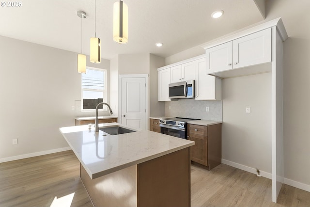 kitchen featuring a sink, white cabinetry, hanging light fixtures, appliances with stainless steel finishes, and a center island with sink