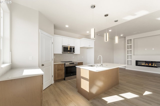 kitchen with a kitchen island with sink, a sink, white cabinets, light countertops, and appliances with stainless steel finishes