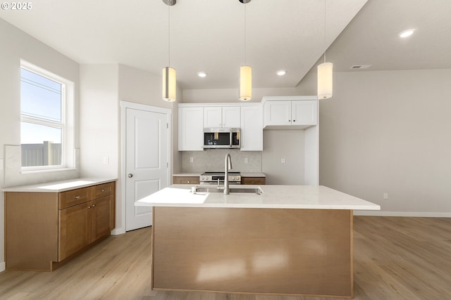 kitchen with pendant lighting, stainless steel microwave, white cabinetry, a sink, and an island with sink