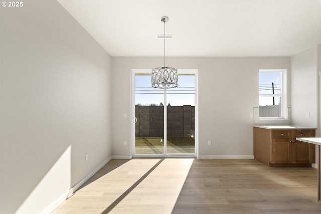 unfurnished dining area featuring light wood finished floors, baseboards, visible vents, and an inviting chandelier