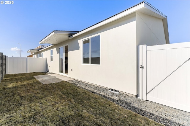 back of house with a fenced backyard, a lawn, and stucco siding