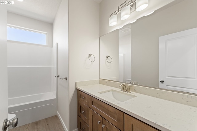 bathroom featuring visible vents, washtub / shower combination, vanity, wood finished floors, and baseboards