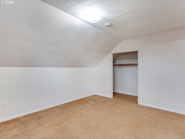 additional living space featuring light carpet, vaulted ceiling, and a textured ceiling