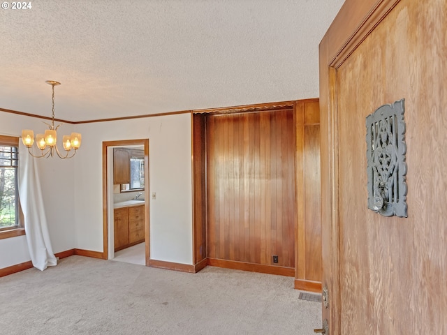 empty room with an inviting chandelier, ornamental molding, light colored carpet, and a textured ceiling