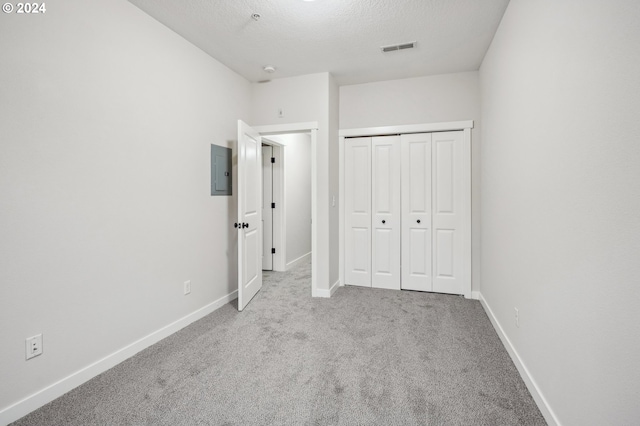 unfurnished bedroom featuring electric panel, a closet, light colored carpet, and a textured ceiling