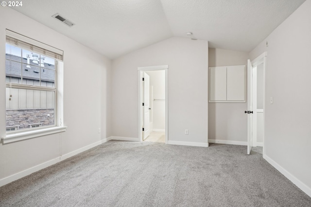 unfurnished bedroom featuring light colored carpet, lofted ceiling, a textured ceiling, and multiple windows