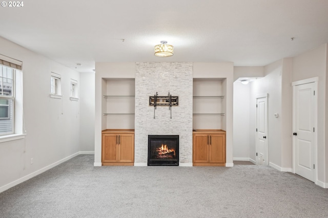 unfurnished living room with a stone fireplace, built in features, and light carpet