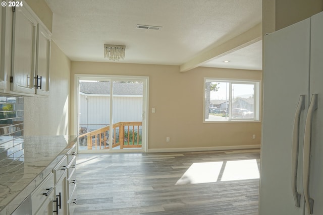 unfurnished dining area with light hardwood / wood-style floors, a notable chandelier, a textured ceiling, and beam ceiling