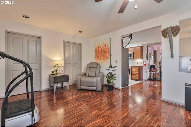 living area with ceiling fan, dark wood-type flooring, and a textured ceiling