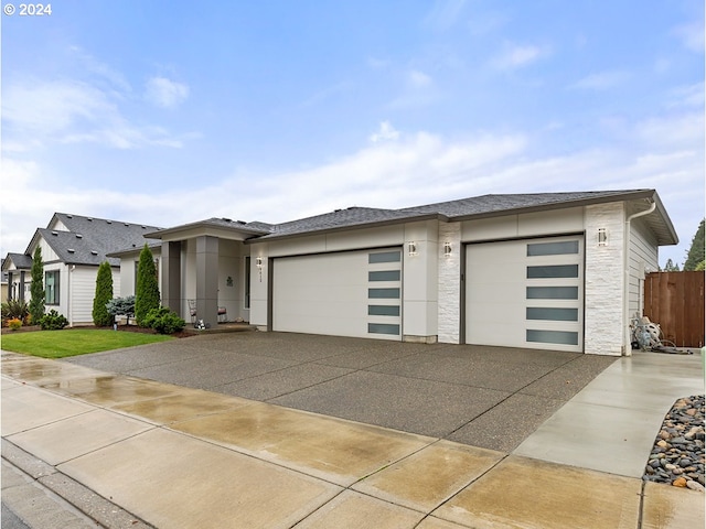 prairie-style house featuring driveway, stone siding, an attached garage, and stucco siding